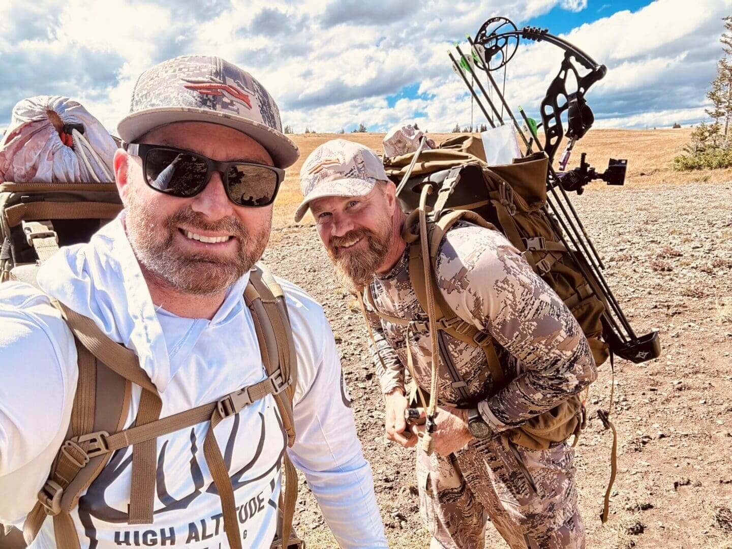 Two men hiking with backpacks and bows.