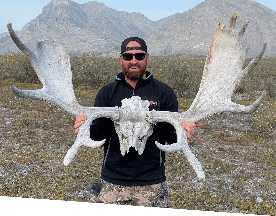 Man holding large antlers in mountainous landscape.